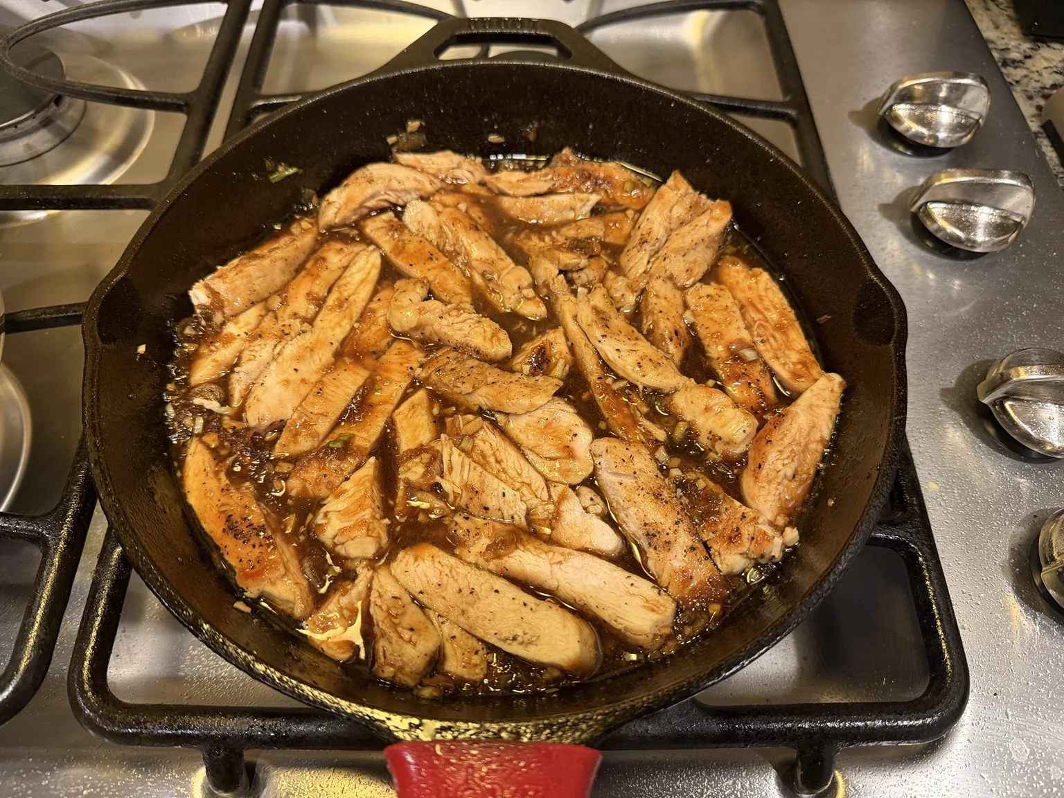 Sliced chicken cutlets coated in teriyaki sauce in a cast-iron skillet.