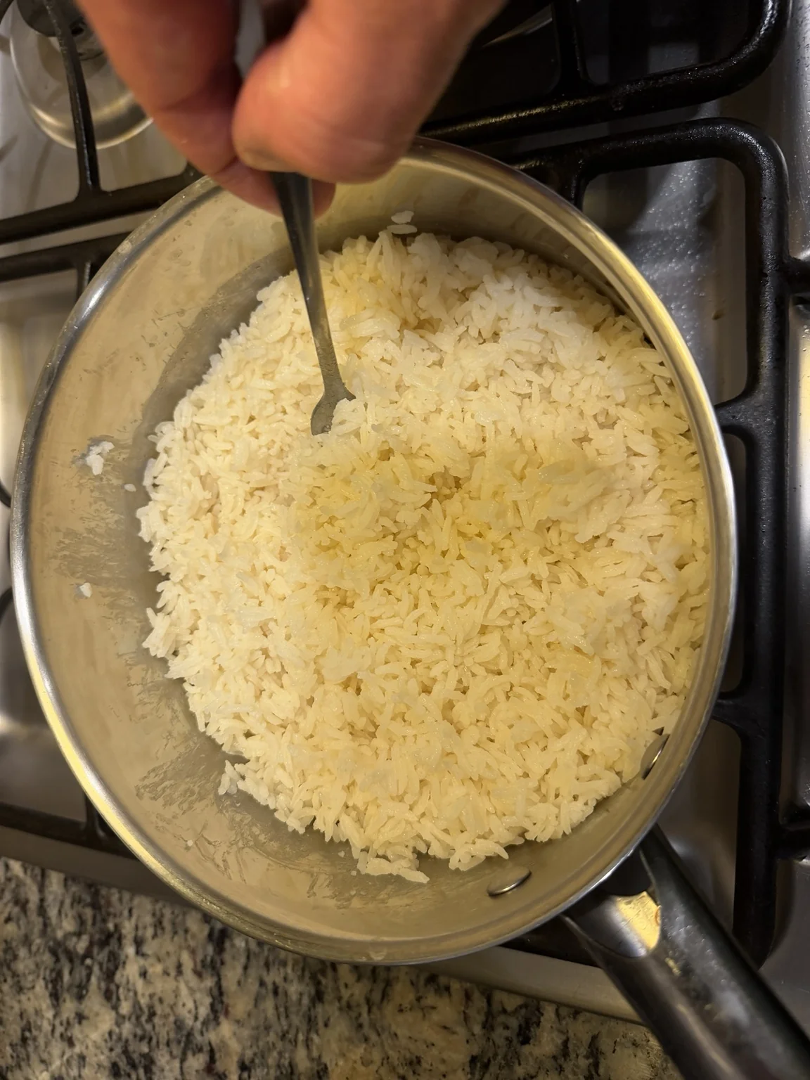 Freshly cooked jasmine rice being fluffed with a fork in a stainless-steel saucepan.