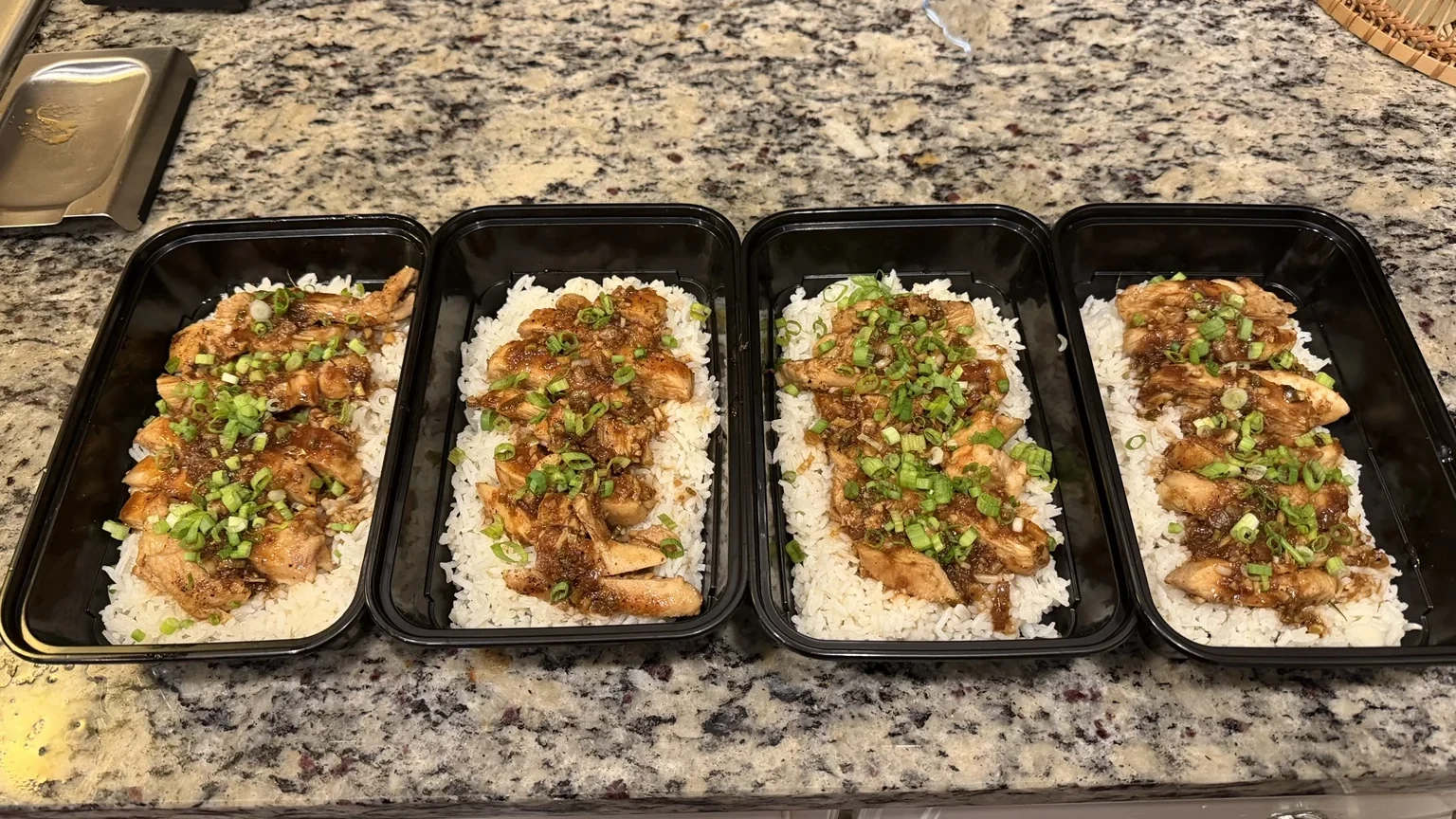 Four meal-prep containers of jasmine rice topped with homemade ginger teriyaki chicken and green onions.
