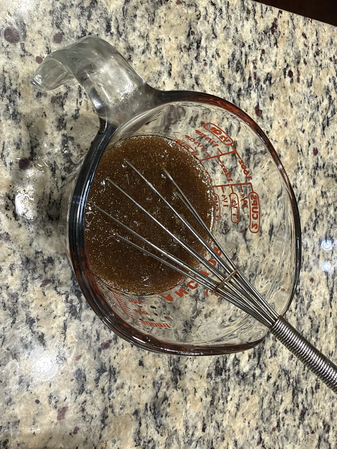 Homemade brown teriyaki sauce in a glass measuring jug with a whisk.