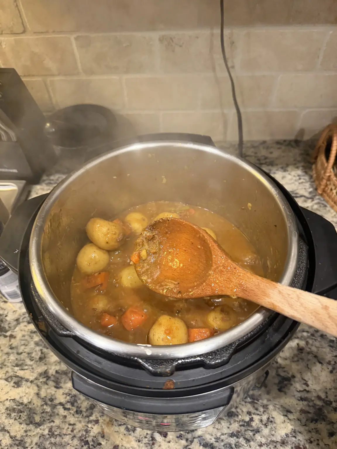 Finished beef stew with whole potatoes and carrots in the Instant Pot with a wooden spoon.