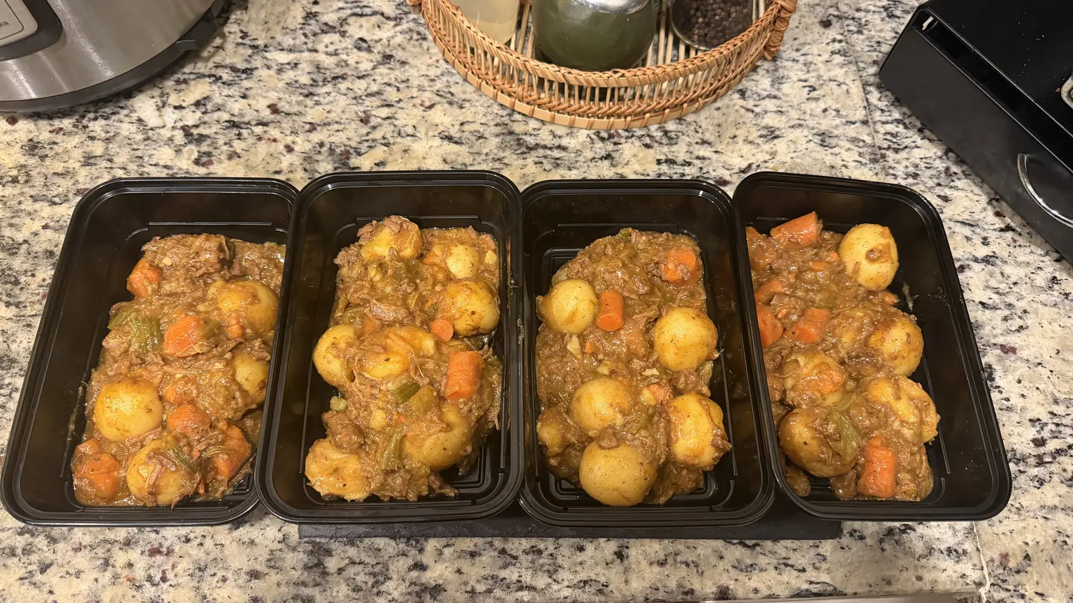 Four black single-compartment meal prep containers filled with beef stew, gold potatoes, and carrots in gravy.