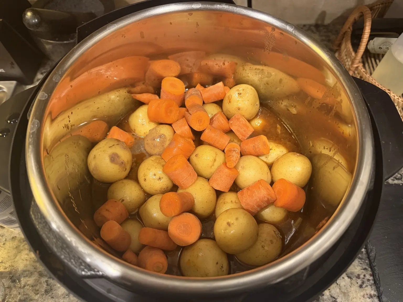 Whole petite gold potatoes and carrot chunks on top of the beef and broth in the Instant Pot.
