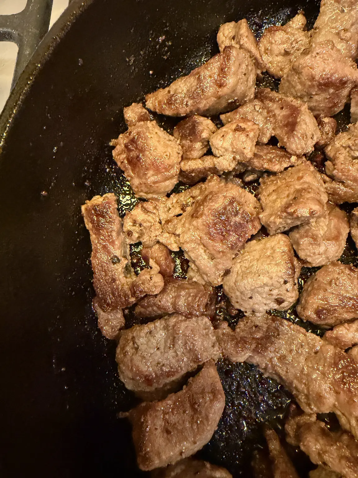 Seared beef stew meat browning in a cast-iron skillet.