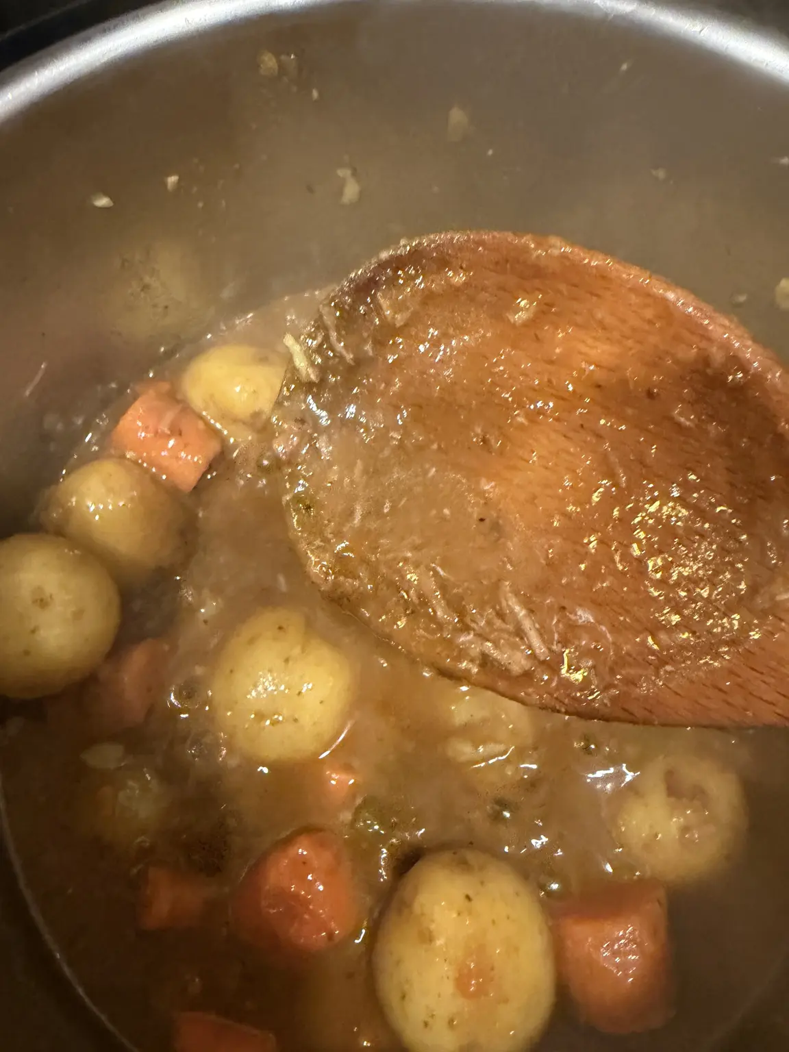 A wooden spoon lifting thickened stew gravy over potatoes and carrots.